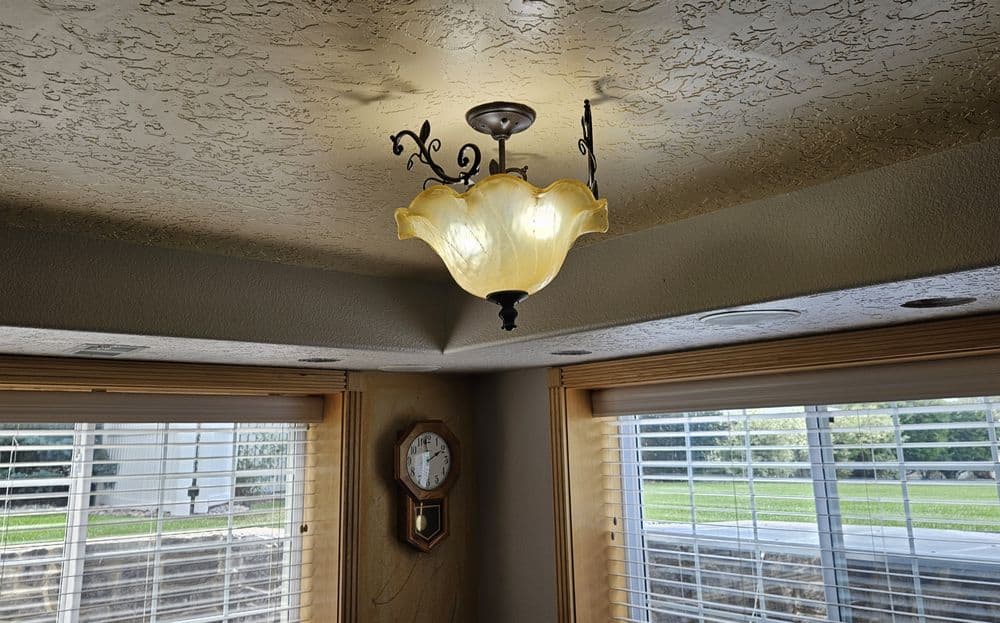 Elegant ceiling lamp with ornate design, illuminating a room with natural light from windows.