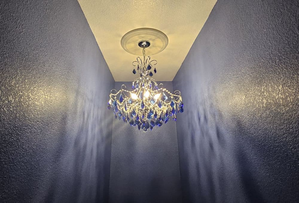 Chic blue crystal chandelier illuminating a textured wall corner. Elegant home decor lighting.