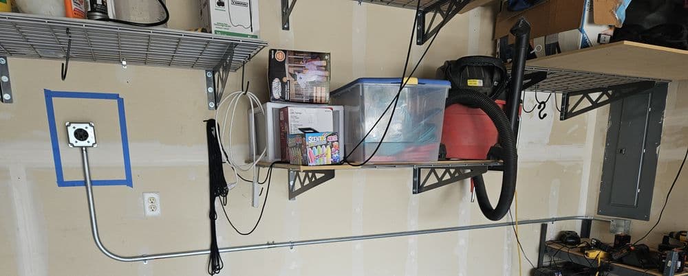 Organized garage with shelves, tools, storage bins, and electrical outlet on the wall.