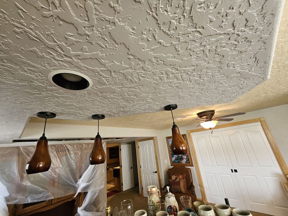 Ceiling with textured finish and pendant lights above a table with mugs and decor items.